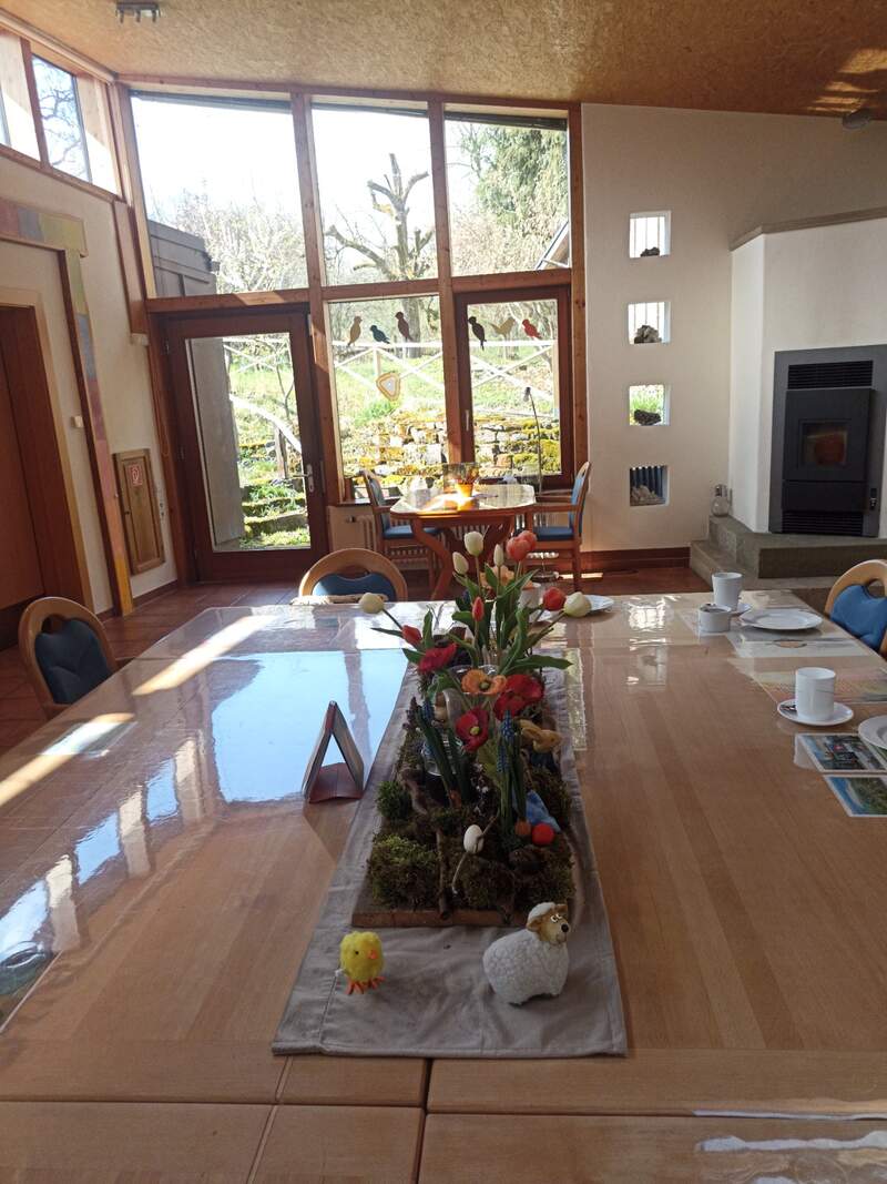 Gemeinschaftsraum Haus Arche – Großer Tisch mit Frühlingsblumen und Blick in den Garten